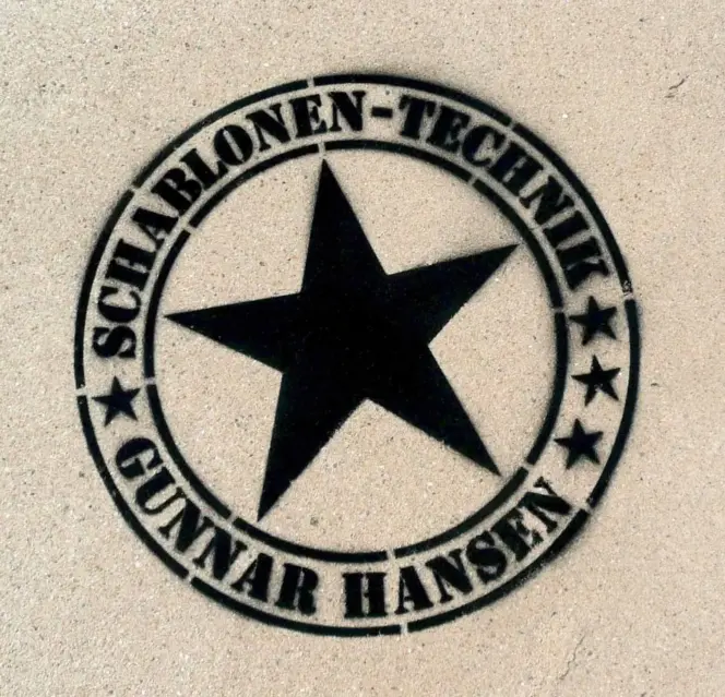 Fertige Kreidespraysignierung des Logos von Schablonen-Technik Gunnar Hansen auf einem Volleyballfeld. Farbe schwarz. Aufnahme direkt von oben