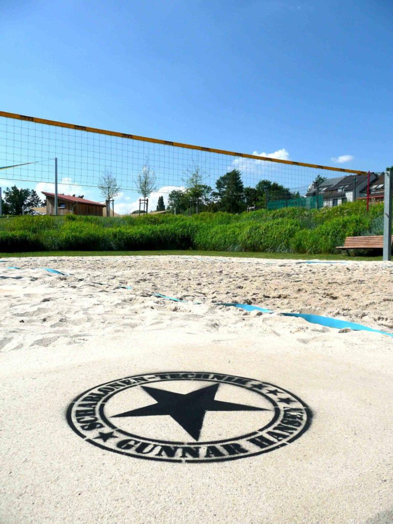 Fertige Kreidespraysignierung des Logos von Schablonen-Technik Gunnar Hansen auf einem Volleyballfeld. Farbe schwarz